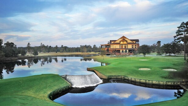 A large, two-story house with a symmetrical facade, situated on a golf course with a pond in the foreground. - The Village at RiverLanding (Wallace)