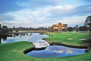 Uma casa grande de dois andares com fachada simétrica, localizada em um campo de golfe com um lago ao primeiro plano.