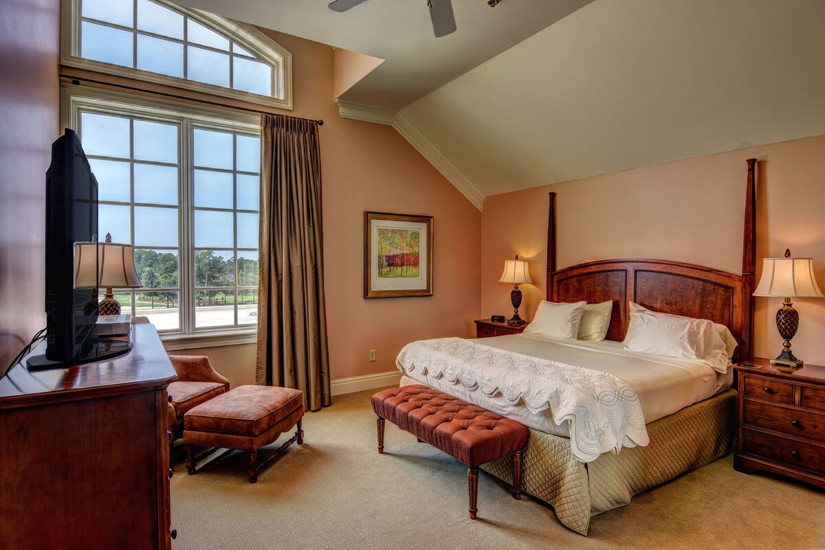 A bedroom with a large window, a bed, a desk, and a chair.