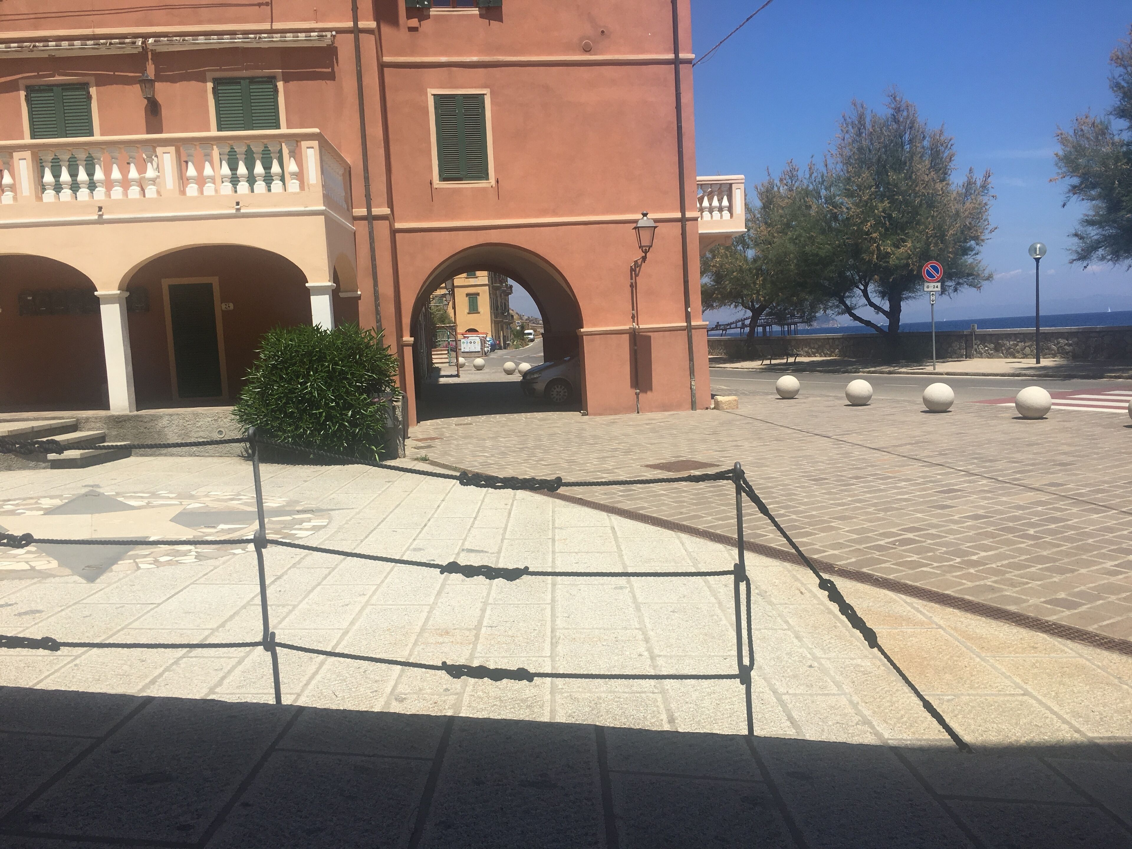 Un edificio con un arco centrale, un cortile lastricato e vista sul mare.