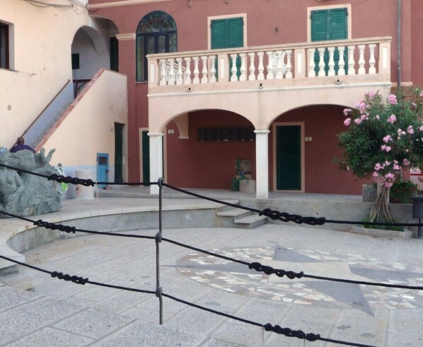 Ein Innenhof mit Steinpflaster, einer Treppe und einem Gebäude mit Rundbogenfenstern und einem Balkon.