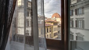 A view through a window with curtains, revealing a building with a dome and adjacent structures.
