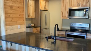 Una cocina moderna con armarios de madera, un refrigerador de acero inoxidable, un microondas y un horno. Hay tres taburetes de bar con asientos de cuero.