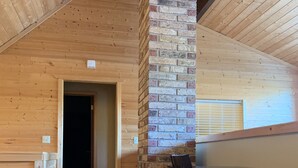Un interior de madera con un pilar de ladrillo, un escritorio con sillas y una puerta que da a otra habitación.