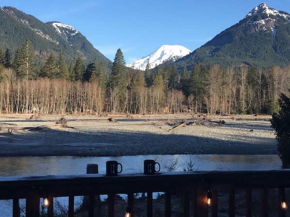 A riverside view with a deck, two mugs, and a mountain in the background.