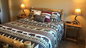 Una cama con un edredón estampado, dos lámparas de noche y una mesita de noche de madera con una lámpara.