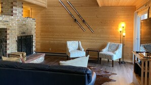 Interior acogedor de una cabaña de madera con chimenea, dos sillones, un sofá y piso de madera.