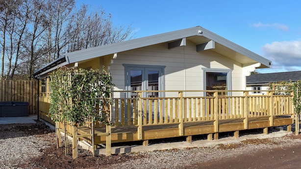 A single-story house with a wooden deck, a small garden, and a clear blue sky.