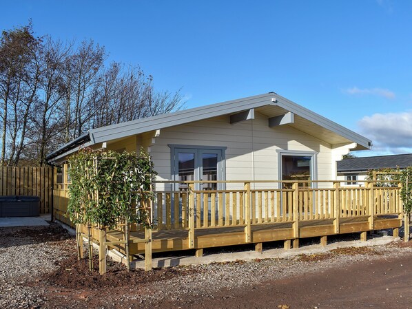 A single-story house with a wooden deck, a small garden, and a clear blue sky.