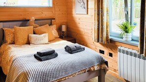 A cozy bedroom with a wooden bed, pillows, a bedside lamp, and a view of the outdoors through a window.