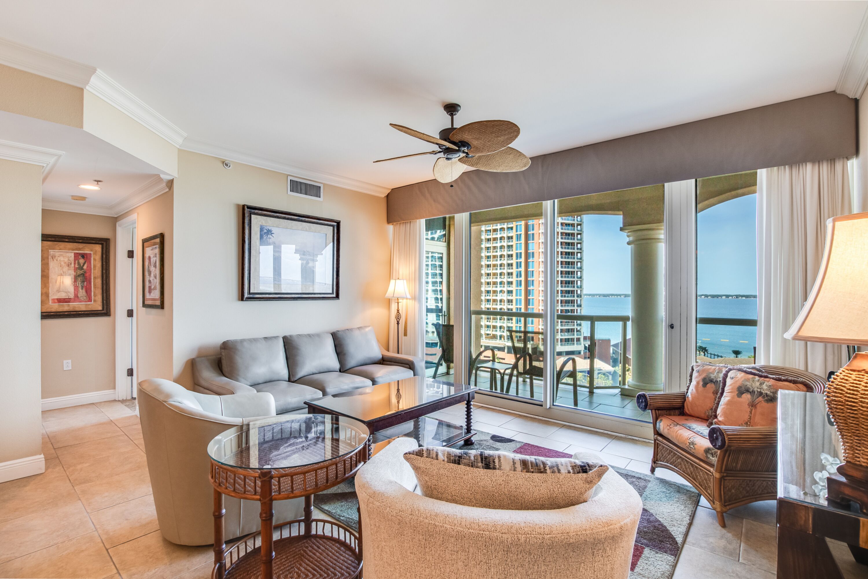 A spacious living room with a balcony, a ceiling fan, and a view of high-rise buildings.