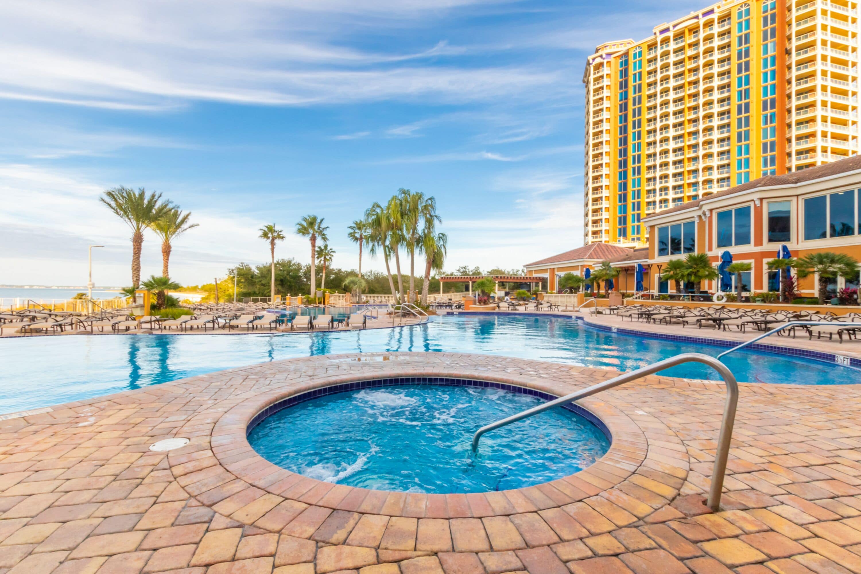 A swimming pool area with lounge chairs and palm trees, surrounded by a tall hotel building.