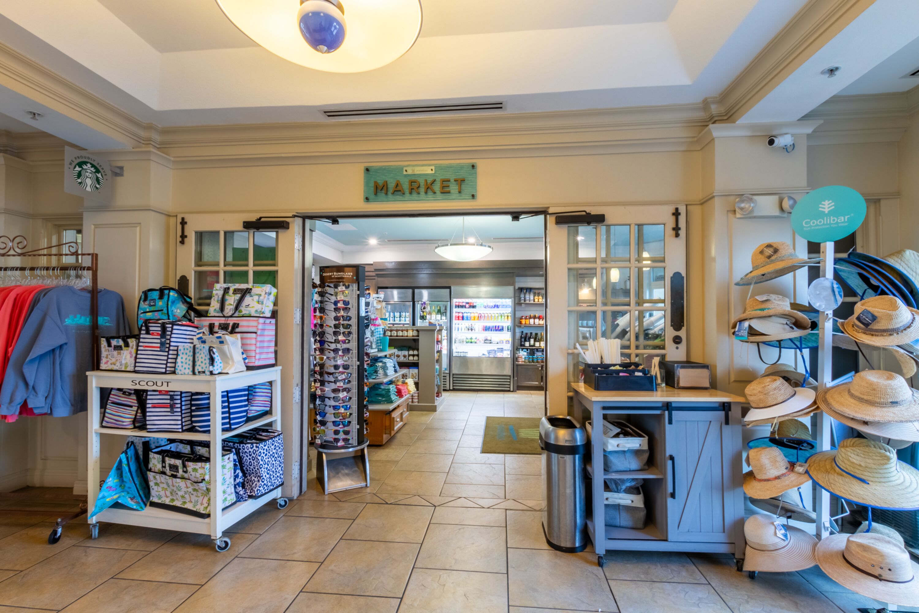 A market area with a sign indicating 'MARKET'. There are shelves with various items, a display of hats, and a 'Coolibar' sign.
