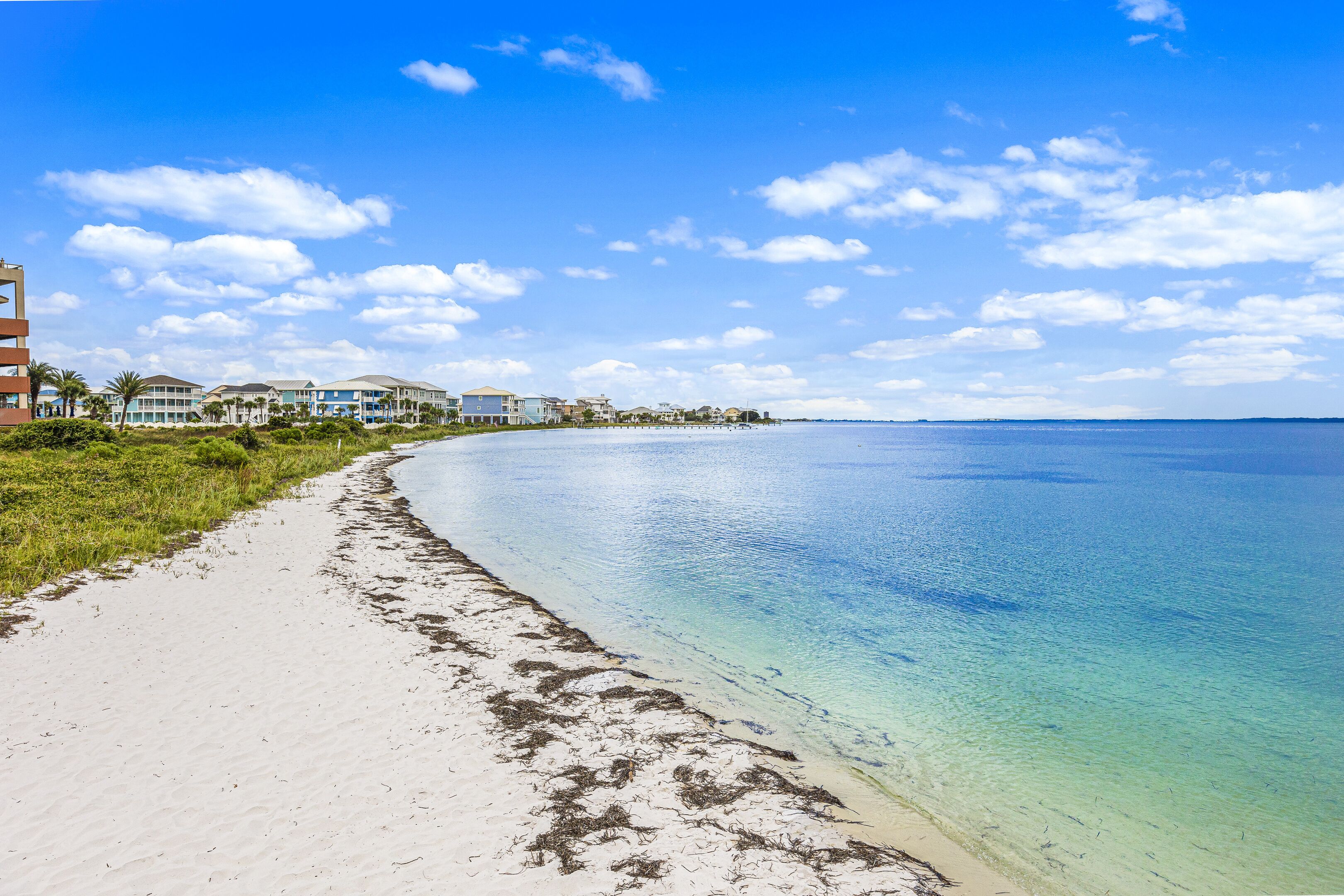 Una playa con agua cristalina, una orilla de arena y edificios al fondo.