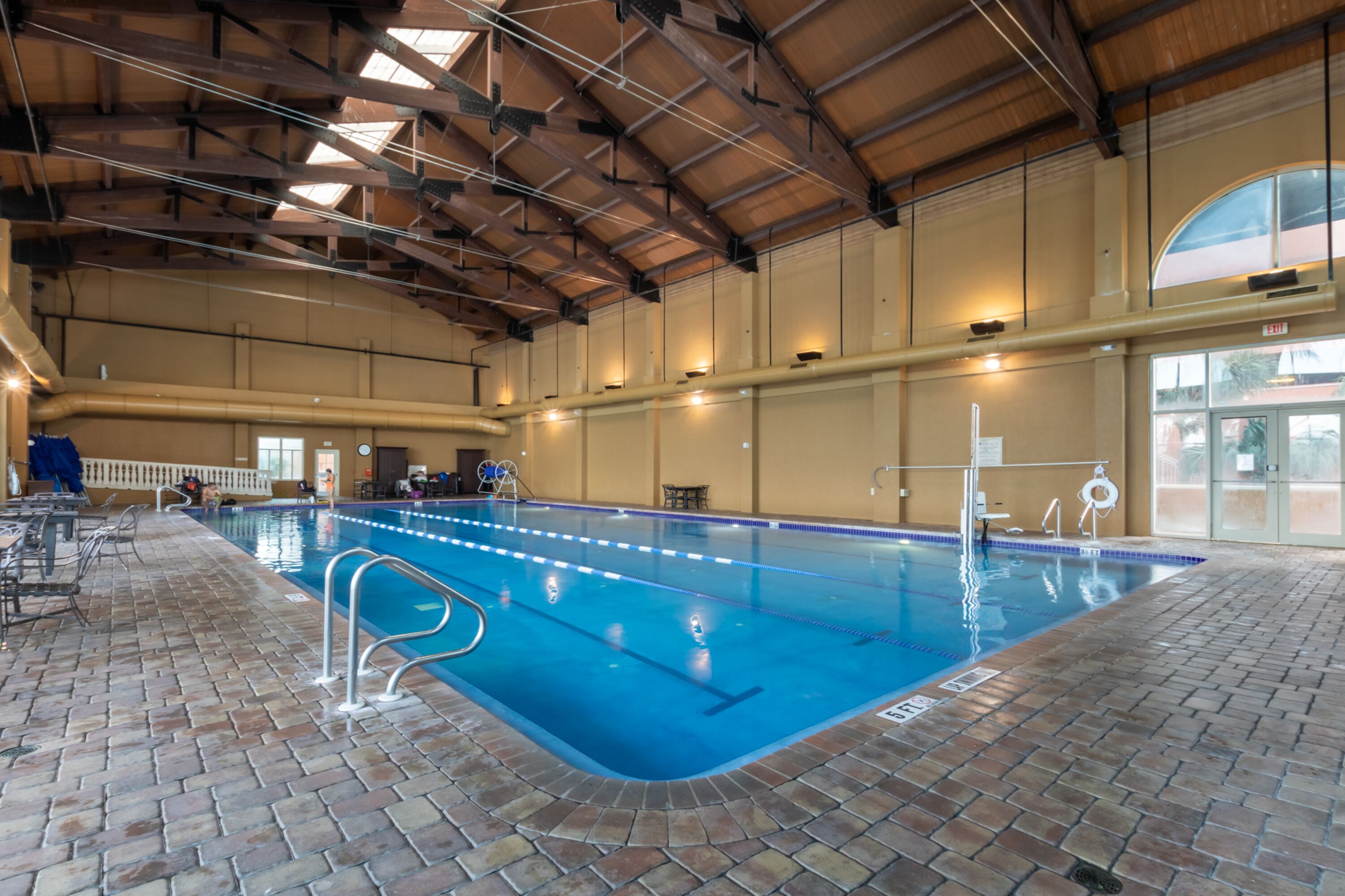 Une piscine intérieure avec des couloirs bien délimités, un sol en briques et un plafond haut avec des poutres apparentes.