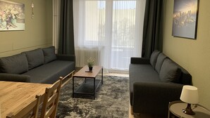 Un salon moderne avec deux canapés gris, une table à manger en bois, une petite table basse et une table d’appoint ronde avec une lampe.