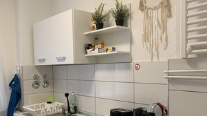 Une cuisine moderne avec un plan de travail blanc, des appareils en acier inoxydable et un attrape-rêves accroché au mur.