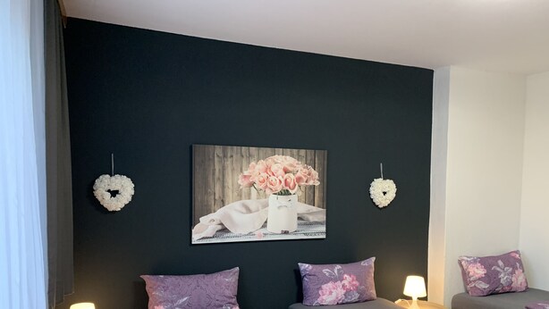 Une chambre d’hôtel avec deux lits, chacun recouvert d’une couvre-lit à motifs floraux et agrémenté d’oreillers assortis. Deux décorations en forme de cœur sont fixées au mur, et un tableau représentant des fleurs est accroché au mur.