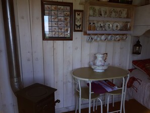 A rustic wooden interior with a white table, a vintage pitcher, and a shelf with decorative plates and glassware. - Meadow Shepherds hut (Rhayader)