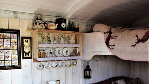 Un intérieur de chalet chaleureux avec un lit superposé, une table avec des chaises, une cheminée et divers objets décoratifs disposés sur des étagères.