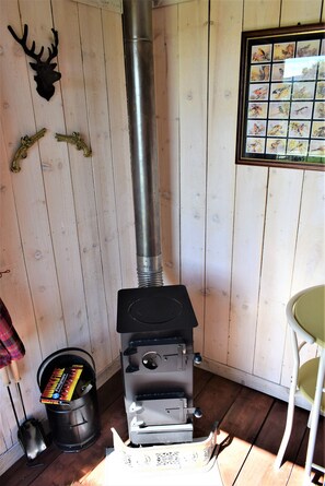 A wood stove with a chimney, a bucket with a box, and a deer head on the wall. - Meadow Shepherds hut (Rhayader)