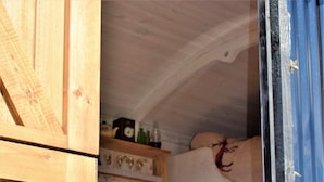 Une pièce rustique en bois, avec un lit superposé, une petite table blanche et des étagères ornées d’objets décoratifs.