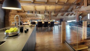 A rustic kitchen with wooden beams, a central island with a sink, and a dining area with chairs and a table. - Chalet Victorina - stunning ski home for 12, close to slopes - OVO Network (La Giettaz)