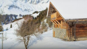 A wooden cabin with a balcony, surrounded by snow-covered mountains and trees. - Chalet Victorina - stunning ski home for 12, close to slopes - OVO Network (La Giettaz)