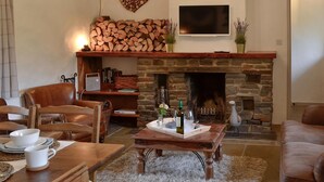 A cozy living room with a stone fireplace, wooden furniture, and a heart-shaped wood art piece on the wall. - 2 bedroom accommodation in Llangennith, near Swansea (Llangennith, near Swansea)