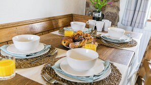 A breakfast table set with white plates, bowls, and cutlery, along with croissants, pastries, and orange juice. - 2 bedroom accommodation in Llangennith, near Swansea (Llangennith, near Swansea)