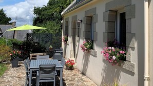 Een stenen terras met een tafel en stoelen, een groene parasol en bloembakken aan een gebouw.