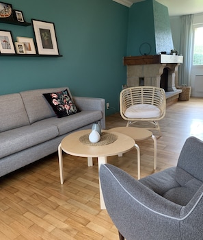 Una sala de estar con un sofá gris, dos mesas redondas y una silla de mimbre.