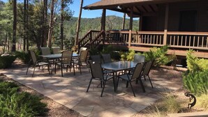 An outdoor patio with a wooden deck, stone flooring, and a table with chairs.