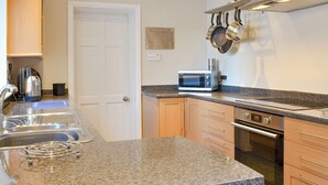Een moderne keuken met granieten aanrechtbladen, roestvrijstalen apparatuur en houten kastjes.