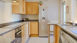 Een compacte keuken met houten kastjes, een ingebouwde oven, een broodrooster, een koelkast, een spoelbak en een wasmachine.