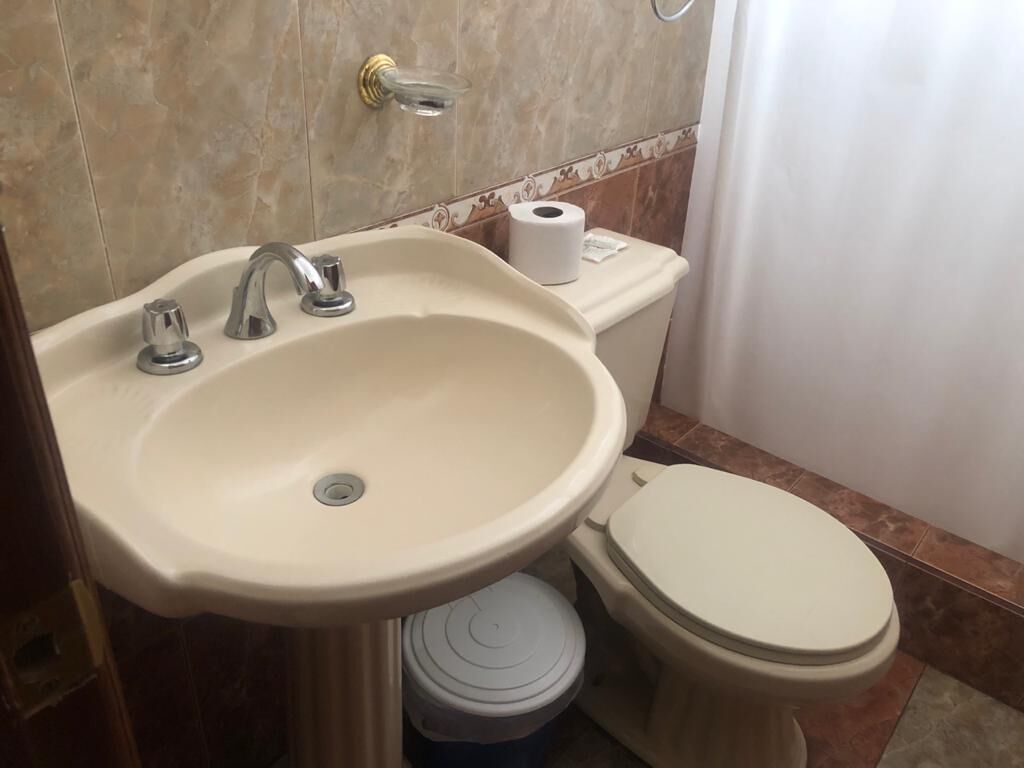 Casa de banho com lavatório, sanita e rolo de papel higiénico na parede.