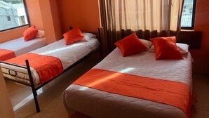 A hotel room with two single beds, each with an orange bedspread and pillows, a large window with a view of buildings, and a curtain. - Hostal La Cocina Tipica (Guayllabamba)