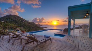 Une terrasse en bois avec des chaises longues et une piscine, le tout offrant une vue sur le coucher de soleil.