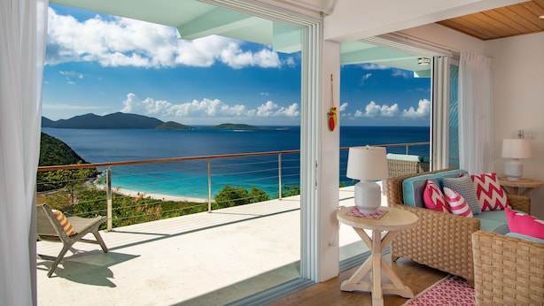 Un balcon avec vue sur l’océan et les montagnes, des meubles en osier et des poissons décoratifs suspendus au plafond.