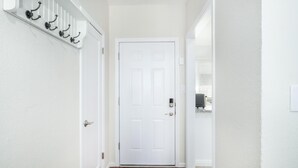A hallway with a white door, a coat rack with hooks, and a small window with blinds. - Fully Refurbished Home for up to 9 Visitors (Fresno)