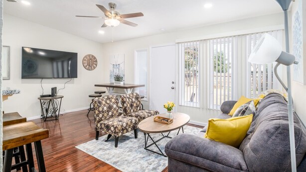 A living room with a ceiling fan, a flat-screen TV, a dining table with chairs, a sofa with cushions, and a window with blinds. - Fully Refurbished Home for up to 9 Visitors (Fresno)