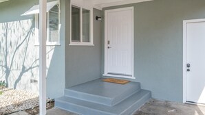 Une maison à l’extérieur gris, avec une porte blanche et un porche doté de marches menant à la porte.