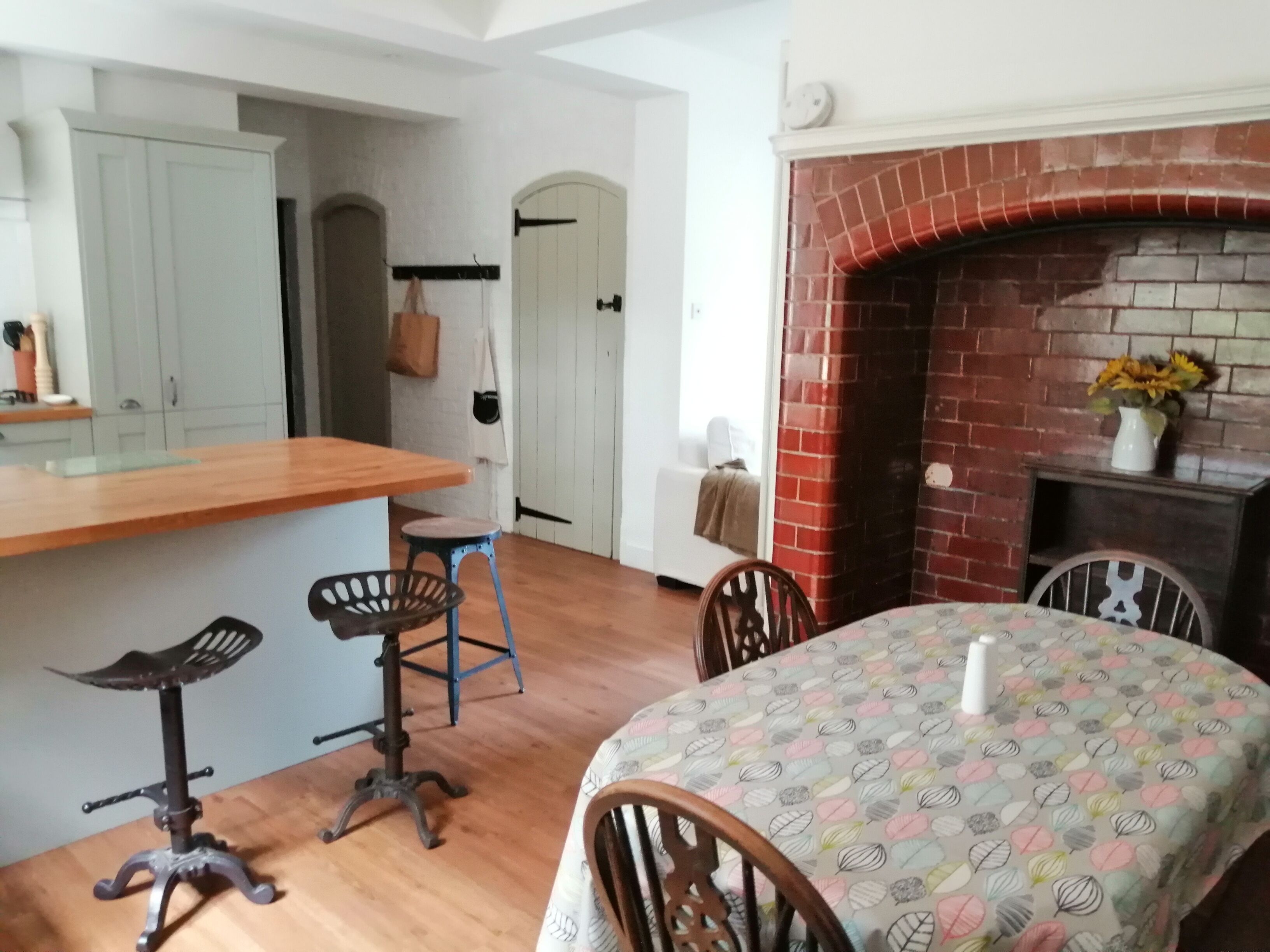 A cozy kitchen with a wooden island, a dining table with a patterned tablecloth, and a brick fireplace.