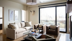 Una sala de estar moderna con un sofá, sillones, una mesa de centro de vidrio y un ventanal con vistas.