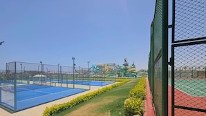 A tennis court with a net, surrounded by a fence, and a water park in the background. - Fantazia Marsa Alam Resort (Marsa Alam)