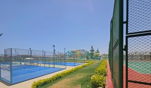 En tennisbane med net, omgivet af et hegn, og en vandpark i baggrunden.