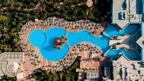 An aerial view of a resort with multiple swimming pools, sun loungers, and palm trees.