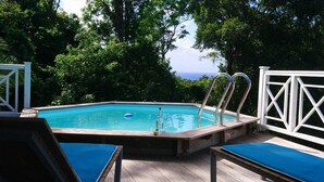 An outdoor swimming pool with a wooden deck, lounge chairs, and a view of the ocean.