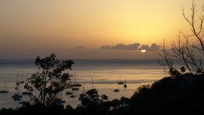 A coastal sunset with boats on calm waters, surrounded by trees and a clear sky.