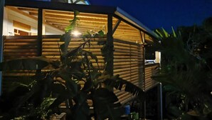 A wooden cabin with a covered porch, surrounded by tropical vegetation.